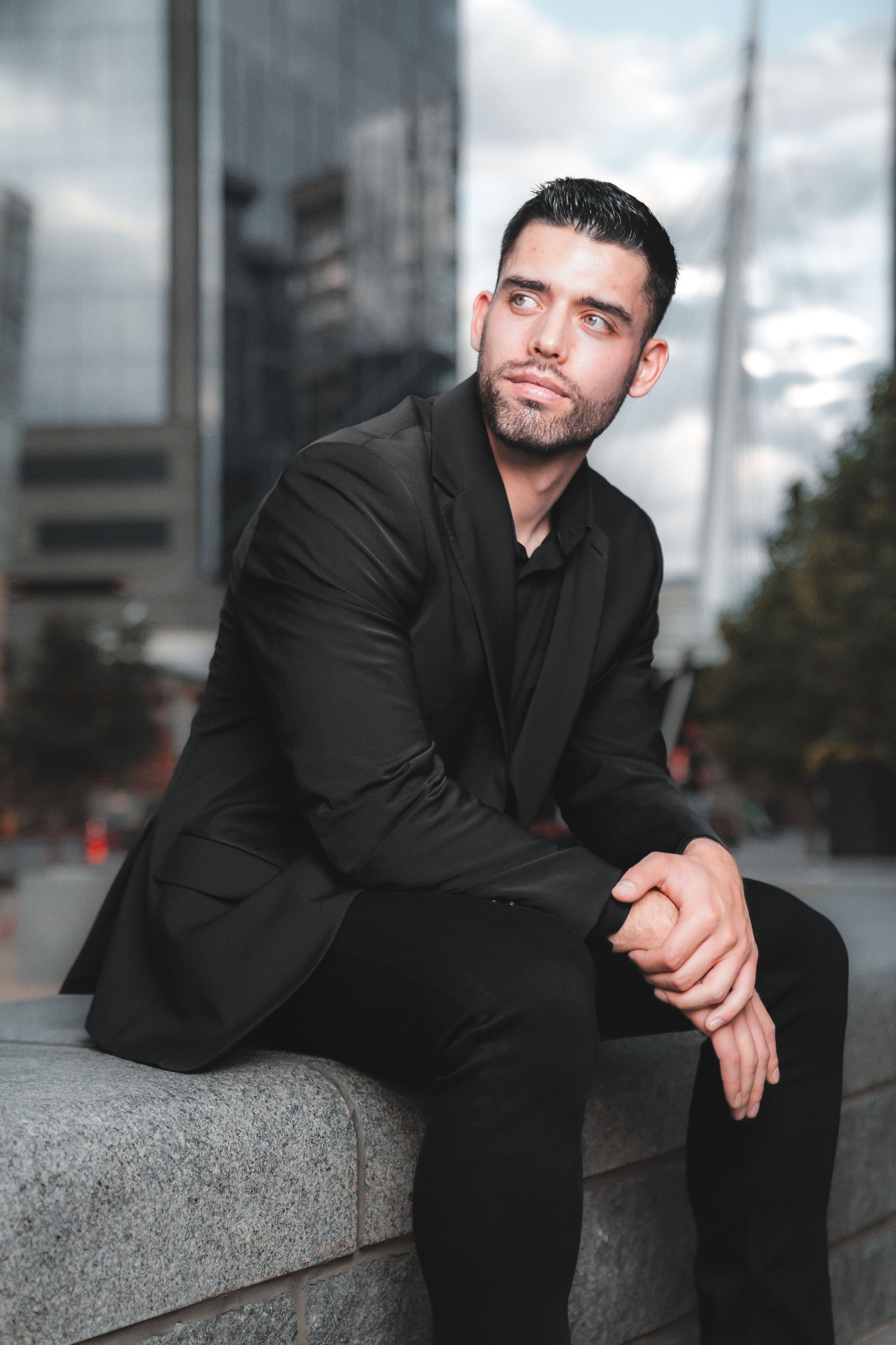 Professional portrait series showing a person in black attire posing against an urban backdrop on a cloudy day.