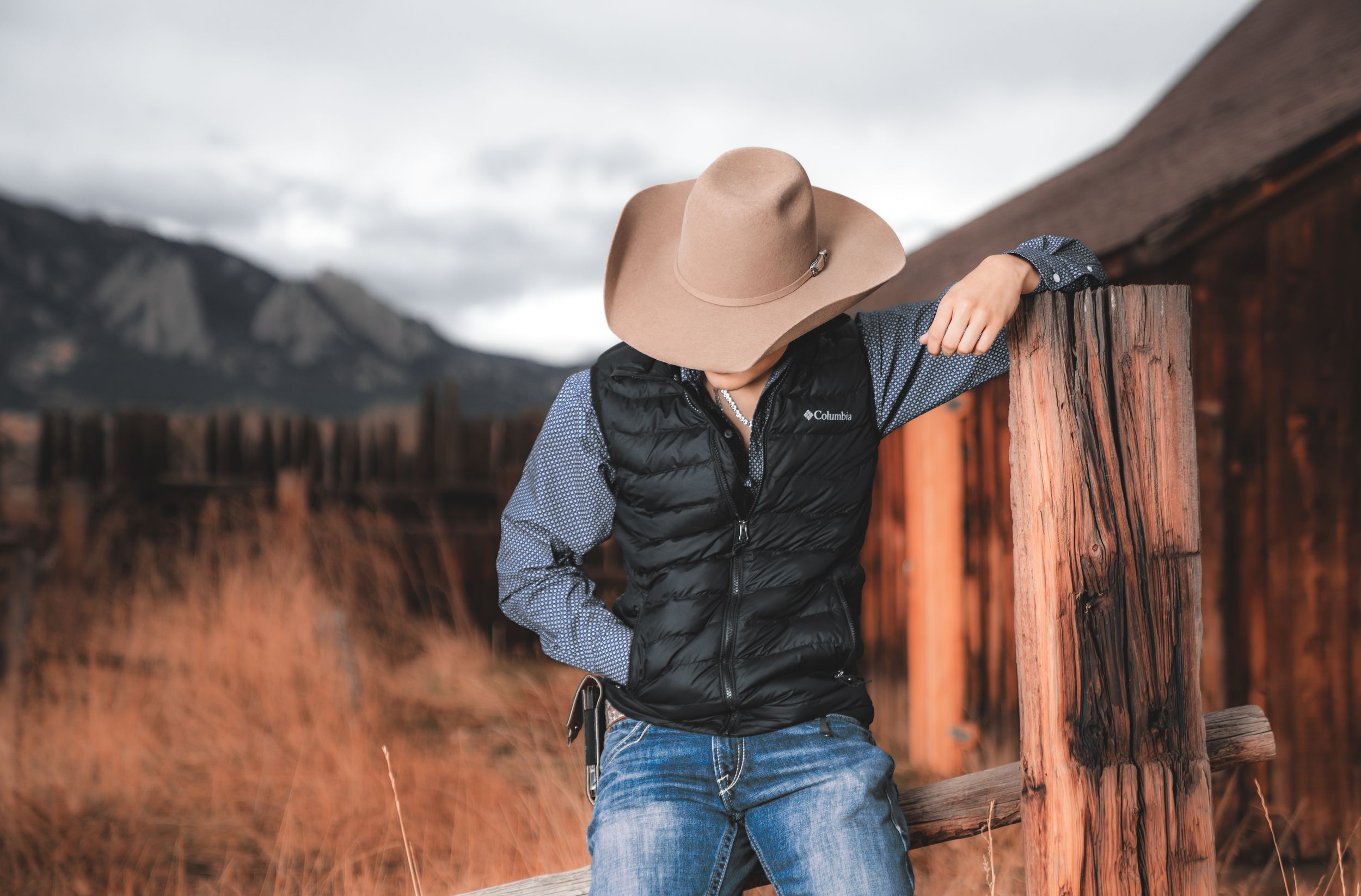 Person in casual wear poses against scenic mountain landscape with autumn colors and rustic wooden structures.
