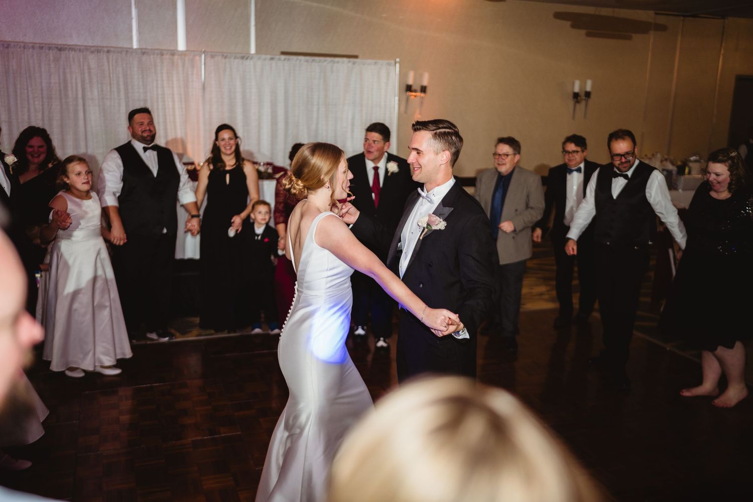 Wedding guests dance and celebrate on a dark dance floor during an evening reception.