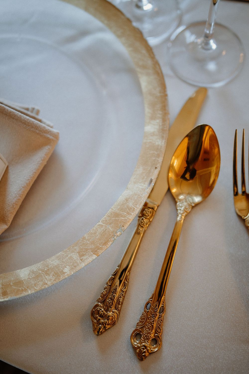 Elegant gold-plated vintage cutlery and fine china plate set against white tablecloth in luxury dining setting.