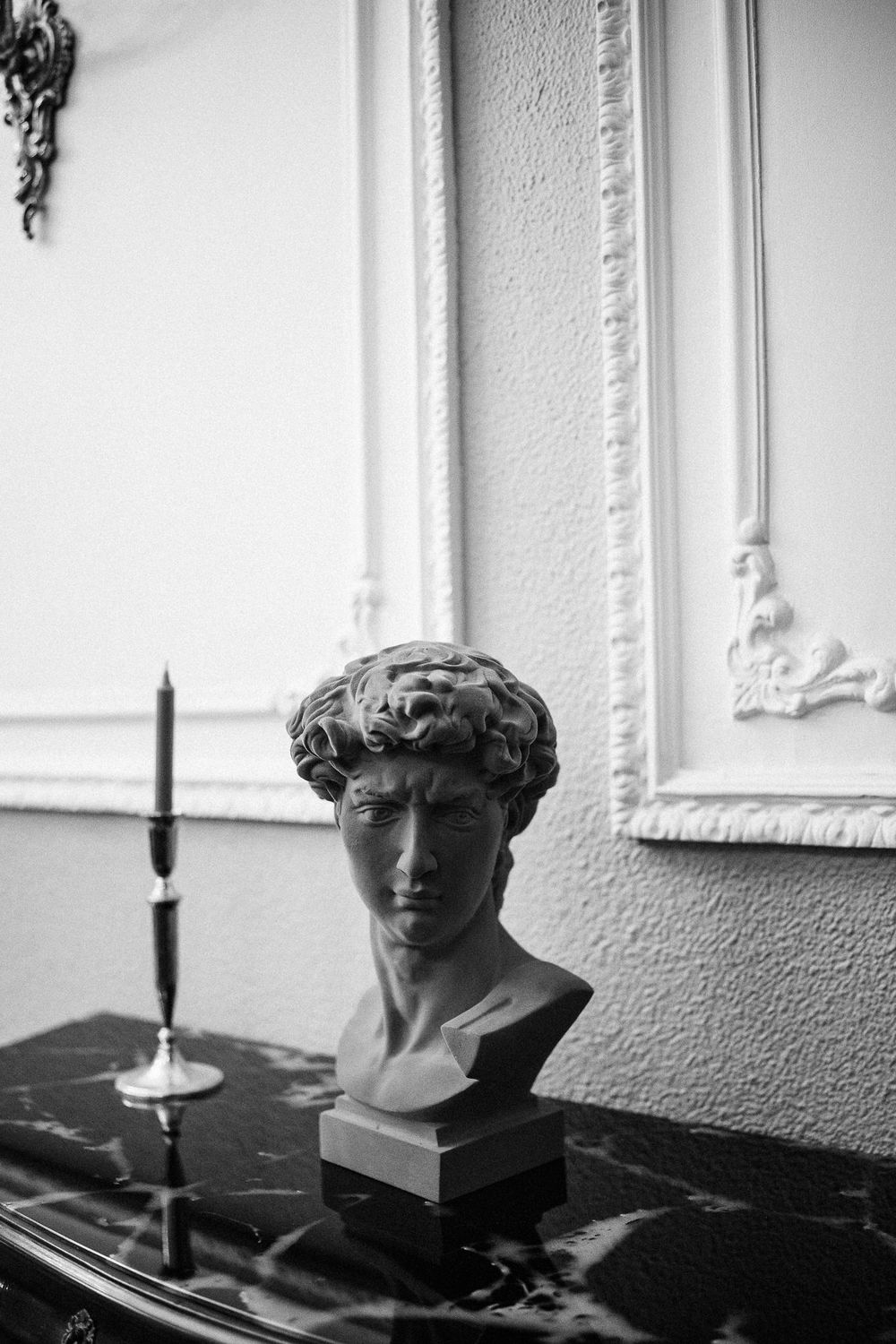 Black and white triptych of a classical bust sculpture with dramatic shadows and candlesticks on display.