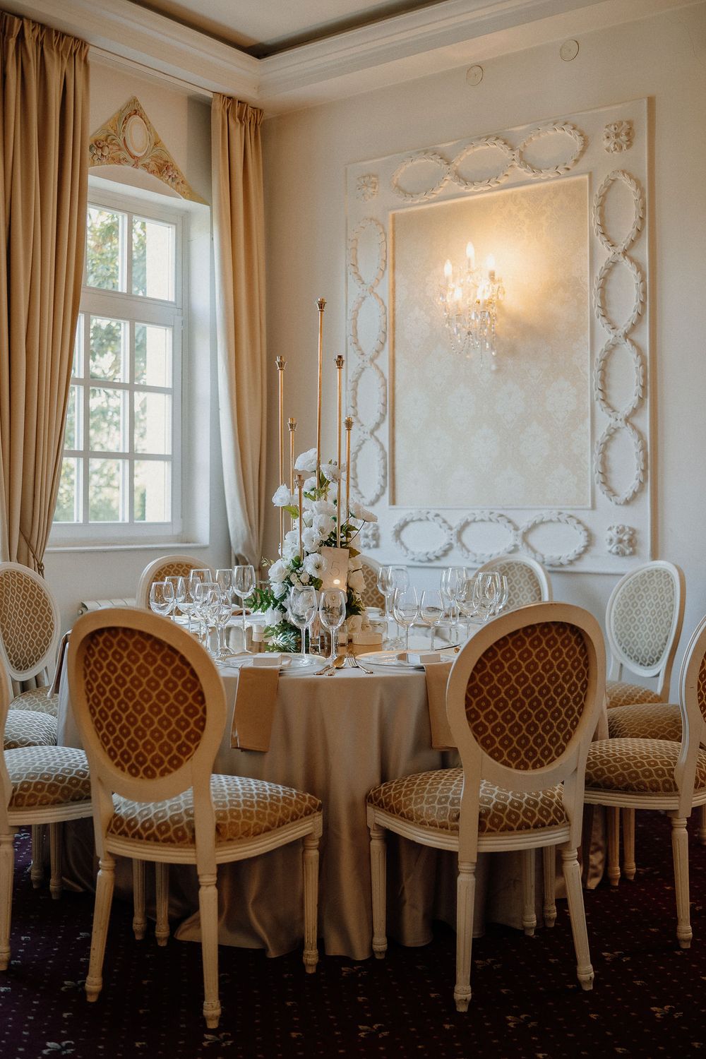 Elegant dining table with vintage French chairs and crystal chandelier in luxurious room with ornate wall moldings.