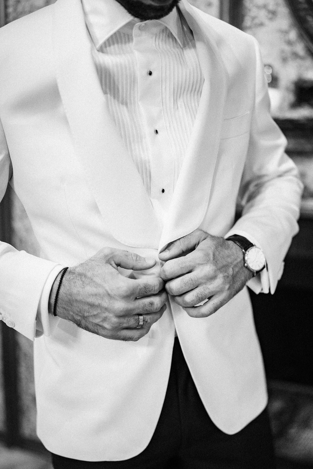 Close-up series of hands adjusting buttons on a crisp white formal tuxedo jacket.