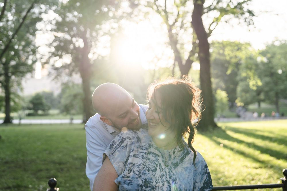A couple shares a tender moment in a sunlit park during golden hour with trees in the background.