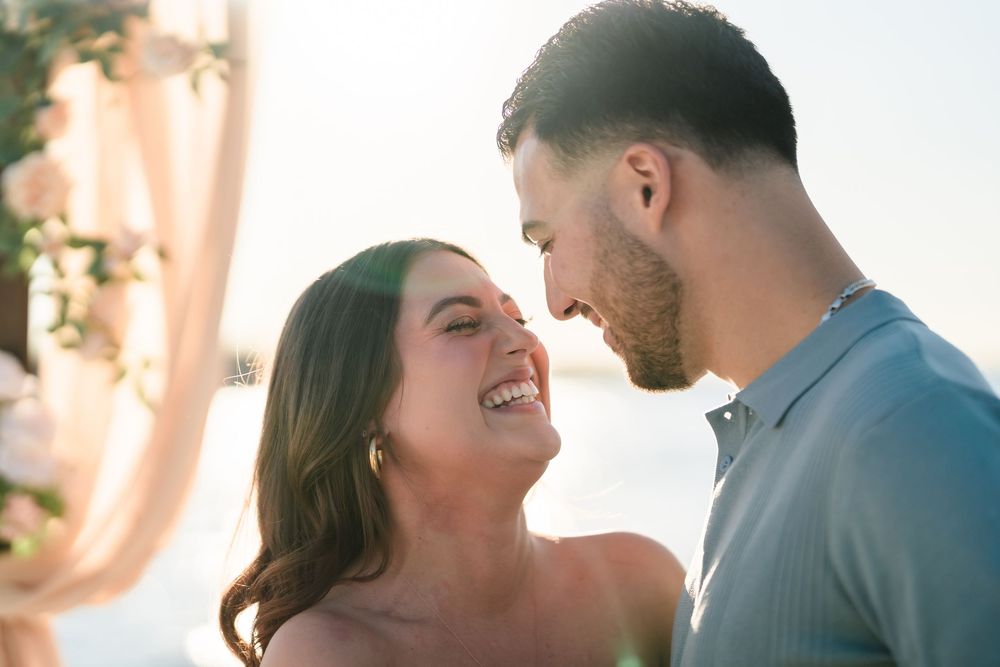 A couple shares a joyful intimate moment together while laughing in warm sunlight.