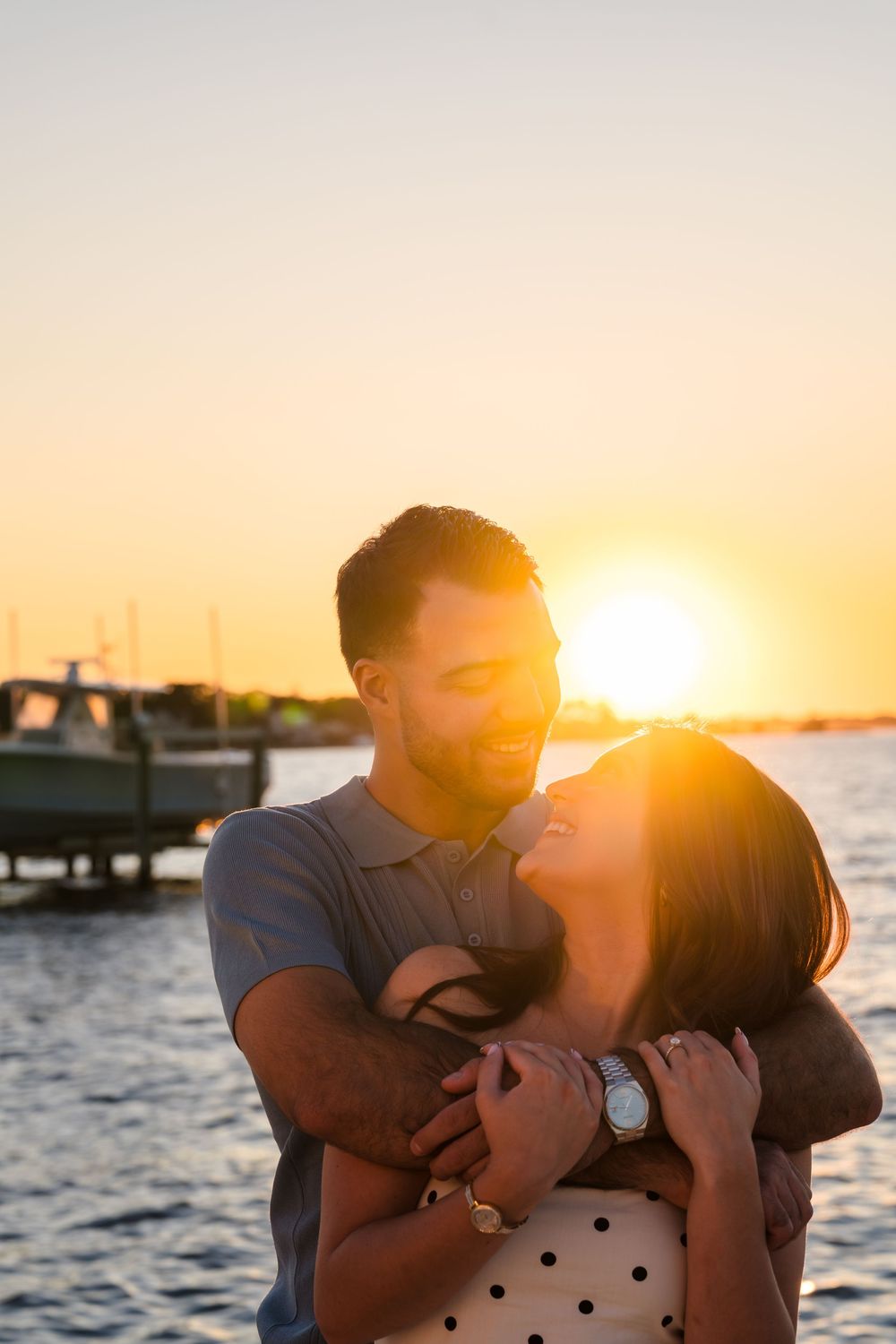 A couple embraces on a pier during a romantic sunset by the ocean with golden light glowing behind them.