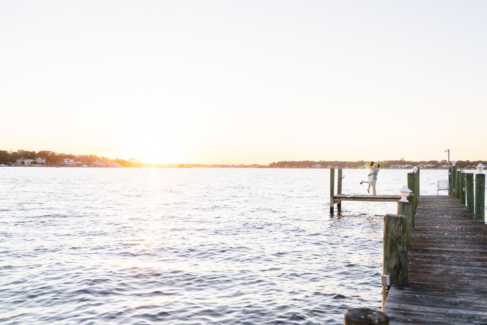 Wooden pier stretches into calm blue waters at sunset with warm golden light reflecting off the ocean surface.