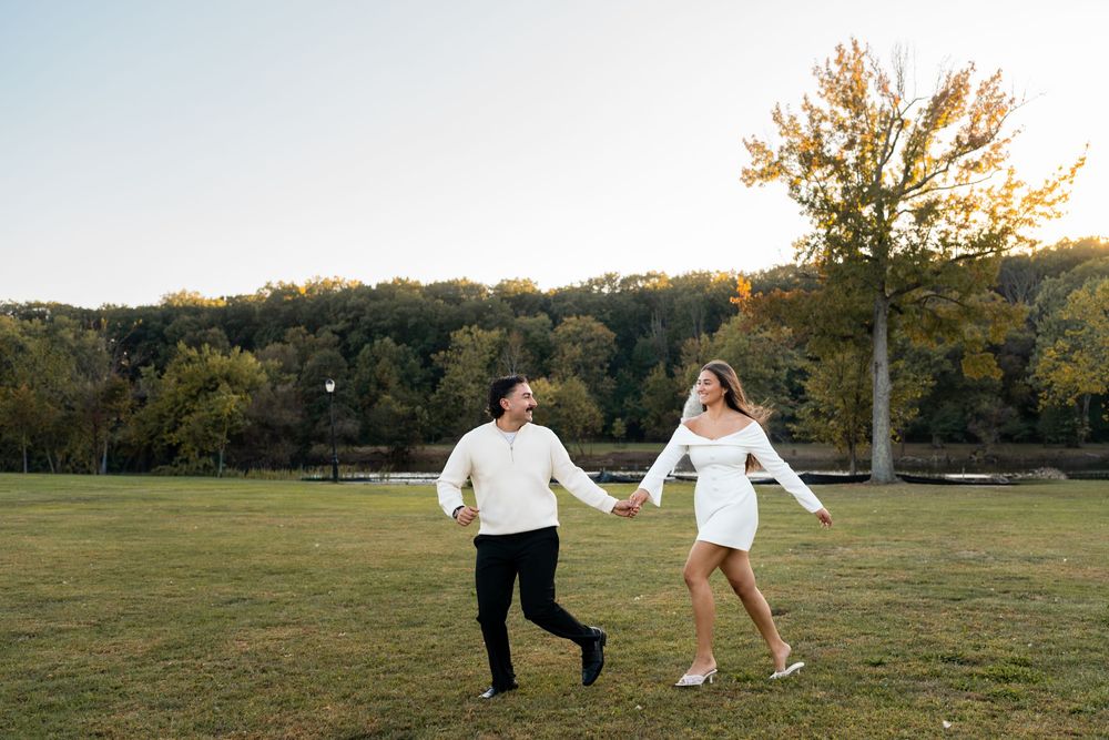Two people hold hands while dancing together in a grassy field at sunset.