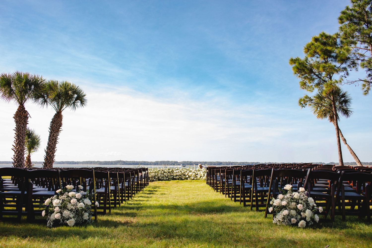Rows of white chairs set up for an outdoor wedding ceremony with palm trees and ocean views.