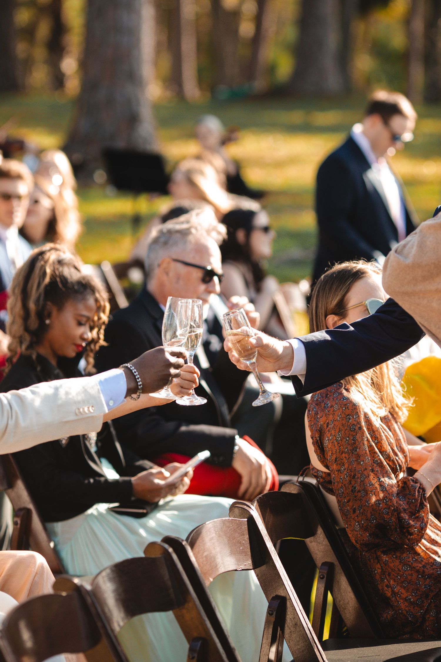 Wedding guests sit in rows of chairs outdoors during a sunny ceremony.