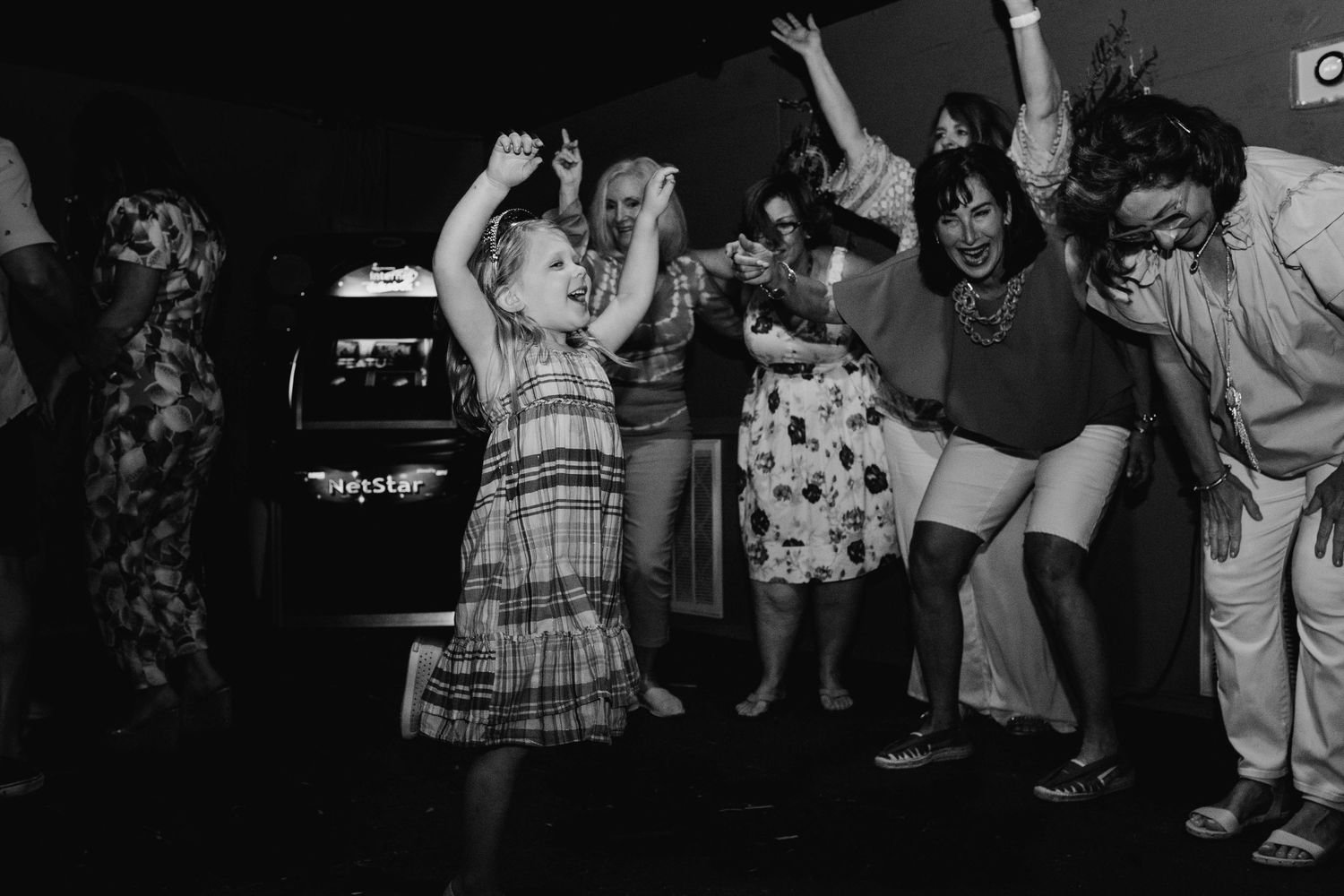 Black and white photo of young child leading a dance in front of older woment at an event session.