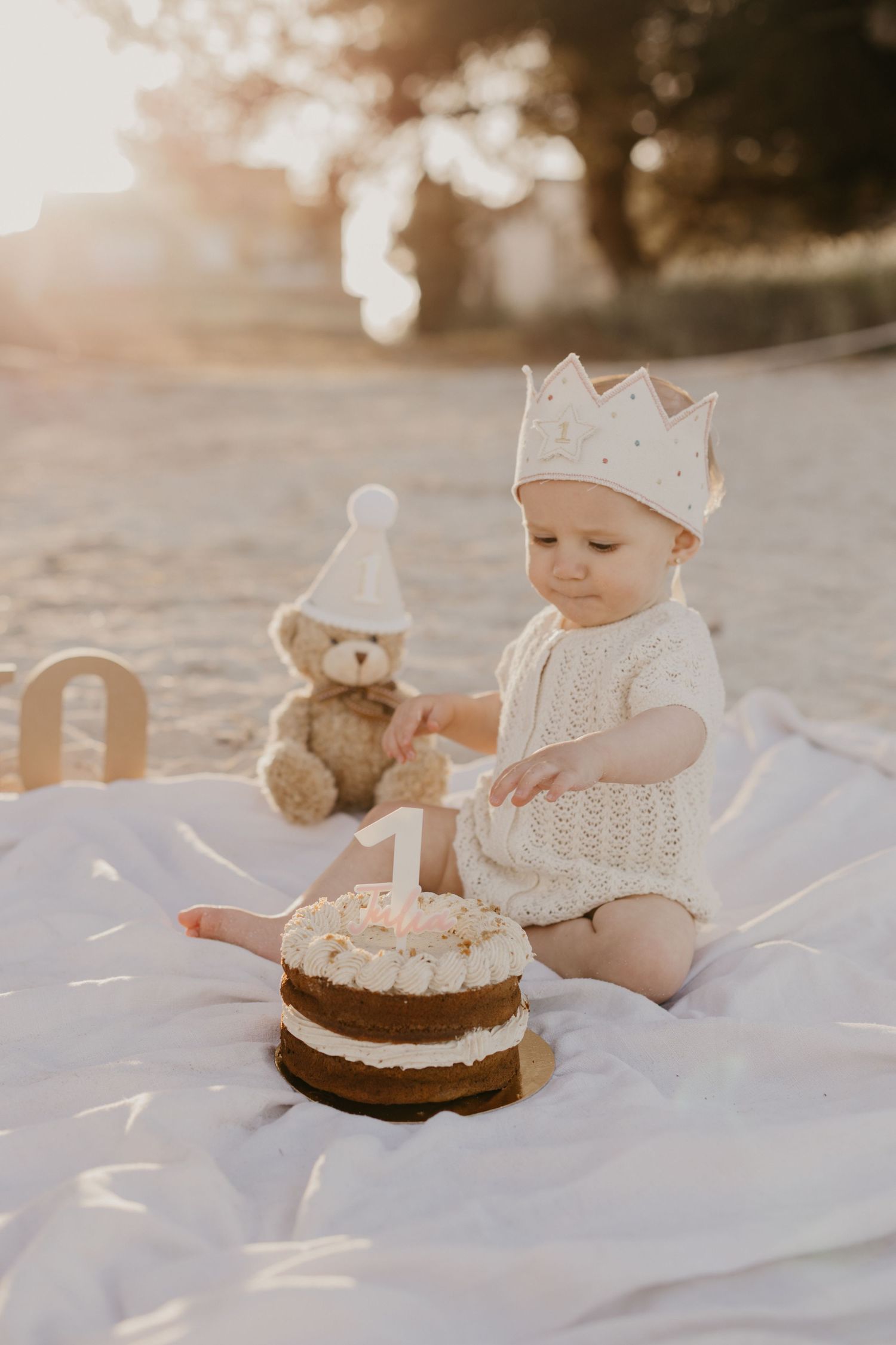 Small child standing on wooden stool wearing white top and patterned shorts against neutral background.