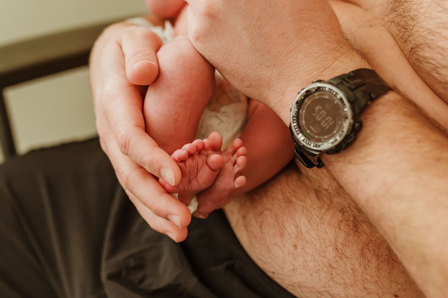 Close-up of hands gently holding and examining a tiny newborn baby's foot against a body