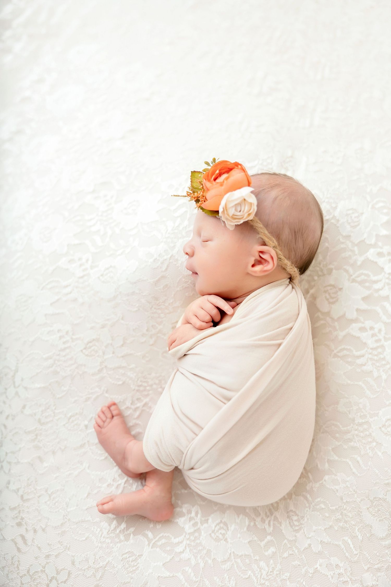 A sleeping newborn in cream wrap with delicate orange floral headpiece lies on white textured backdrop in four similar poses.