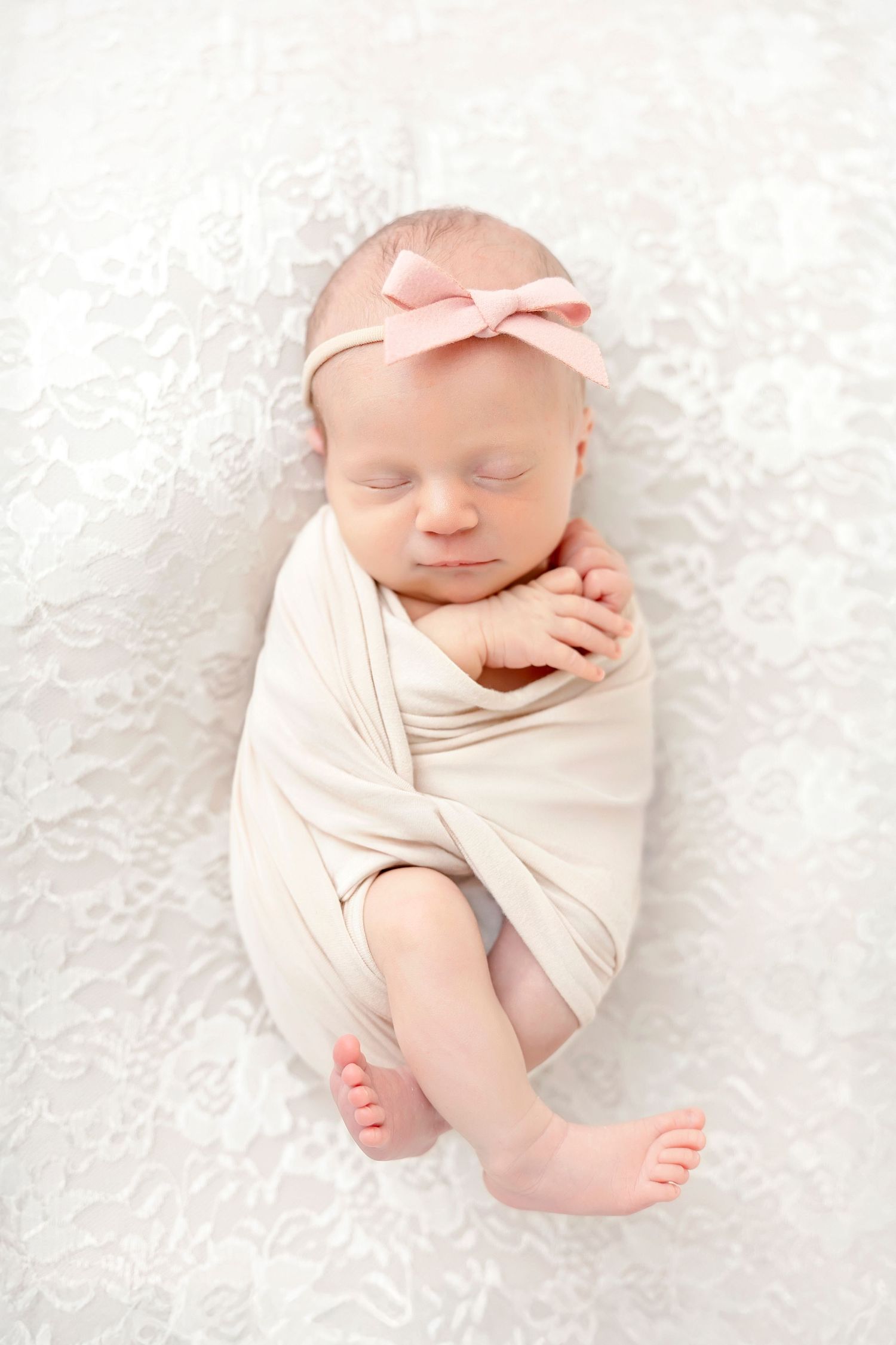 Newborn baby wrapped in soft pink fabric sleeping peacefully on white textured blanket in professional studio setting.