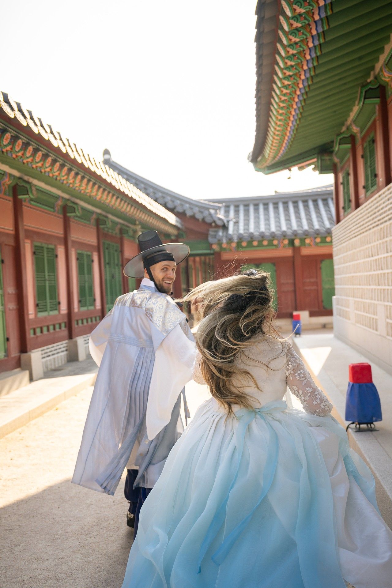 Traditional Korean hanbok dresses flow elegantly against palace architecture at Gyeongbokgung Palace in Seoul.