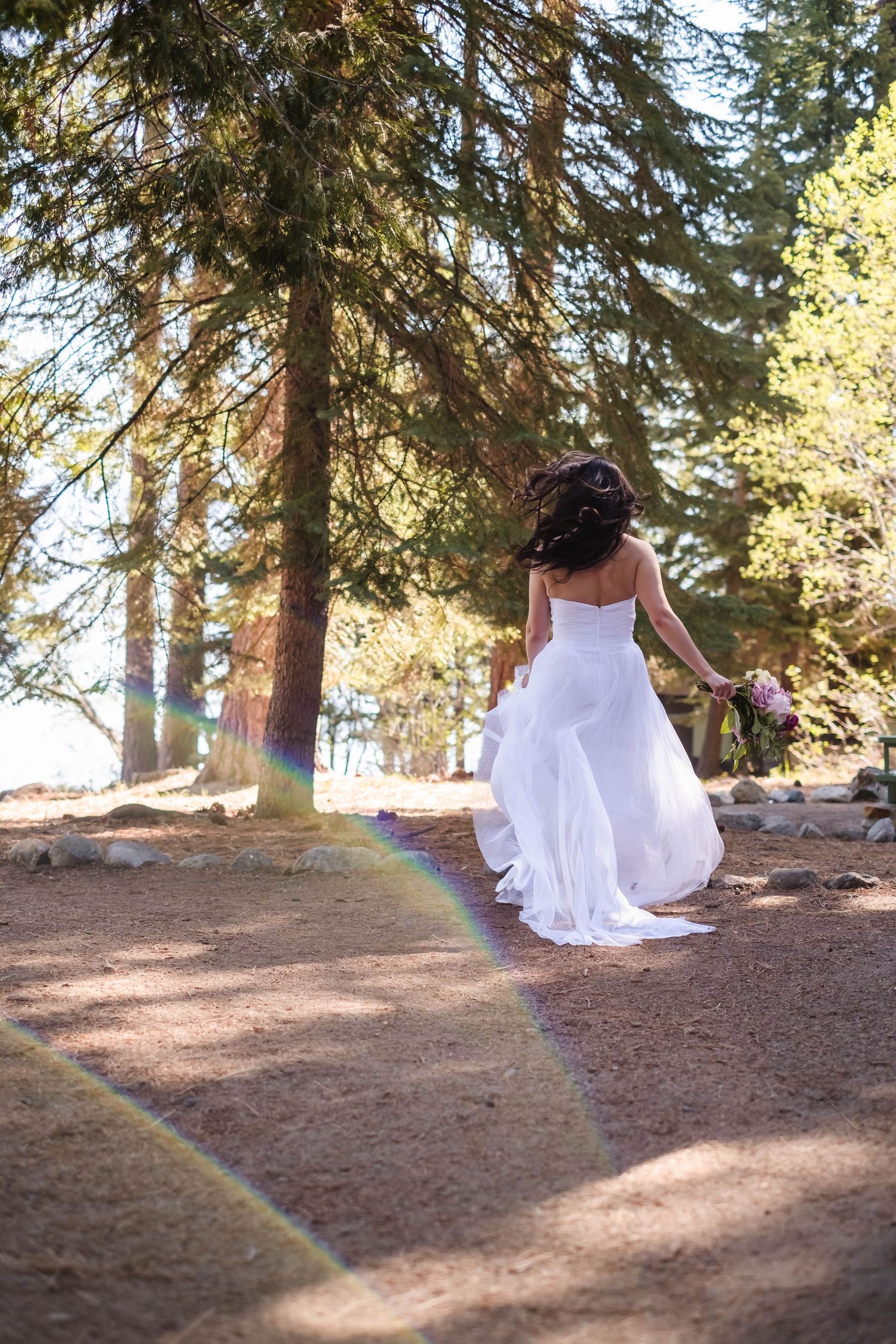 A person in a flowing white dress spins gracefully among tall pine trees in the forest along the shore of lake tahoe.