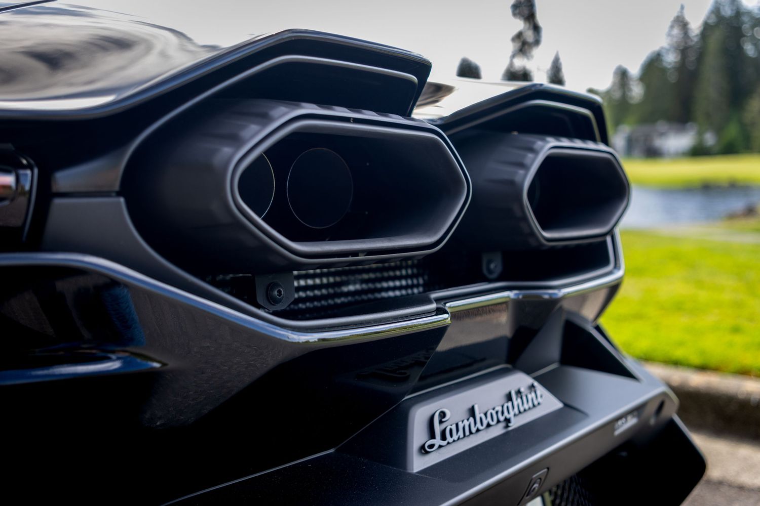 Close-up view of black Lamborghini exhaust pipes and rear diffuser details showing aggressive supercar styling.