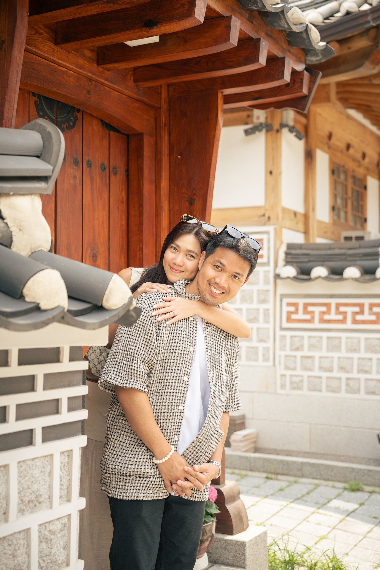 A couple embraces while wearing matching gingham outfits at a traditional Korean hanok building with wooden beams.