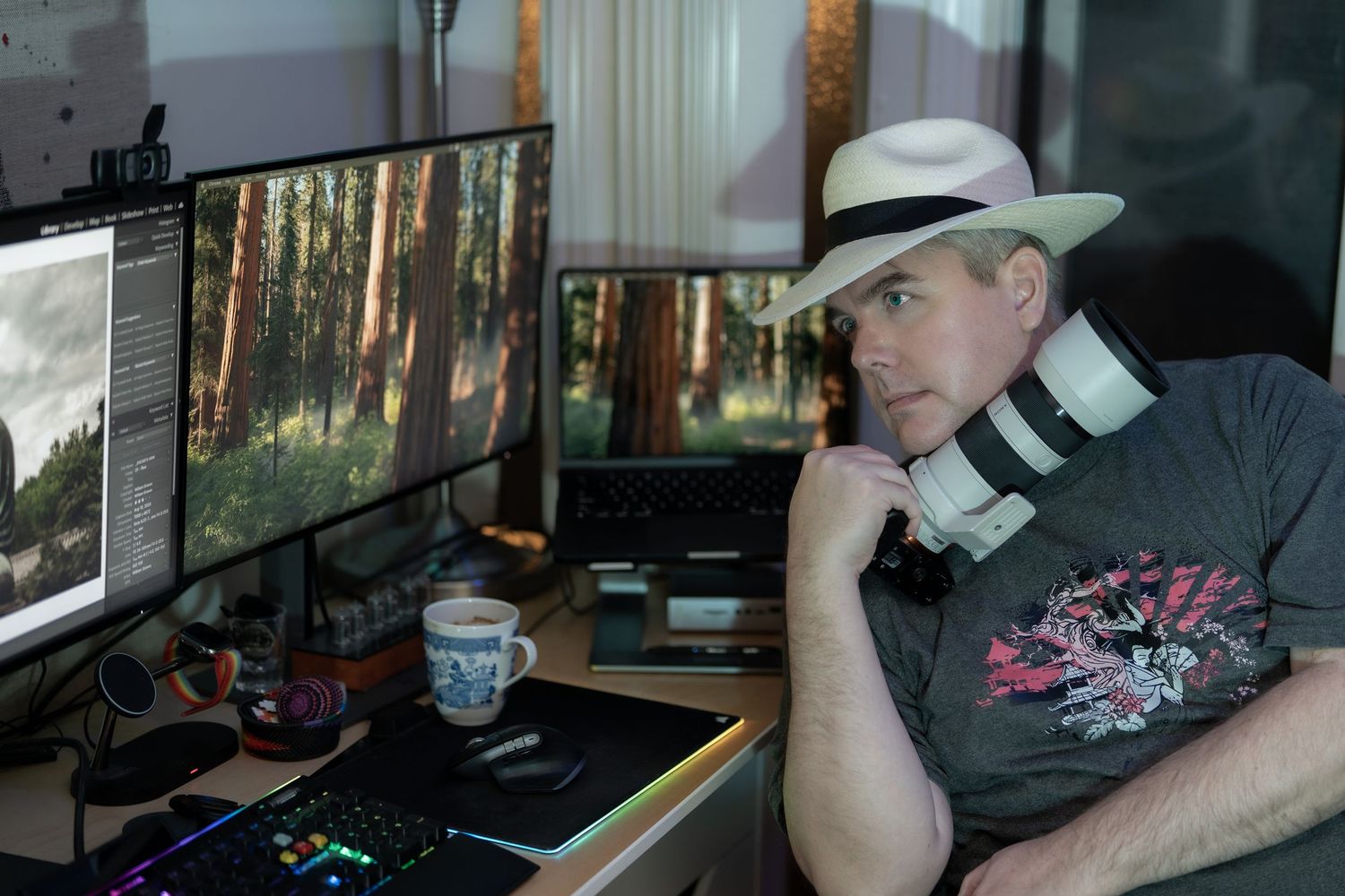 A person wearing a white baseball cap sits at a computer workstation with multiple monitors in a dimly lit room.