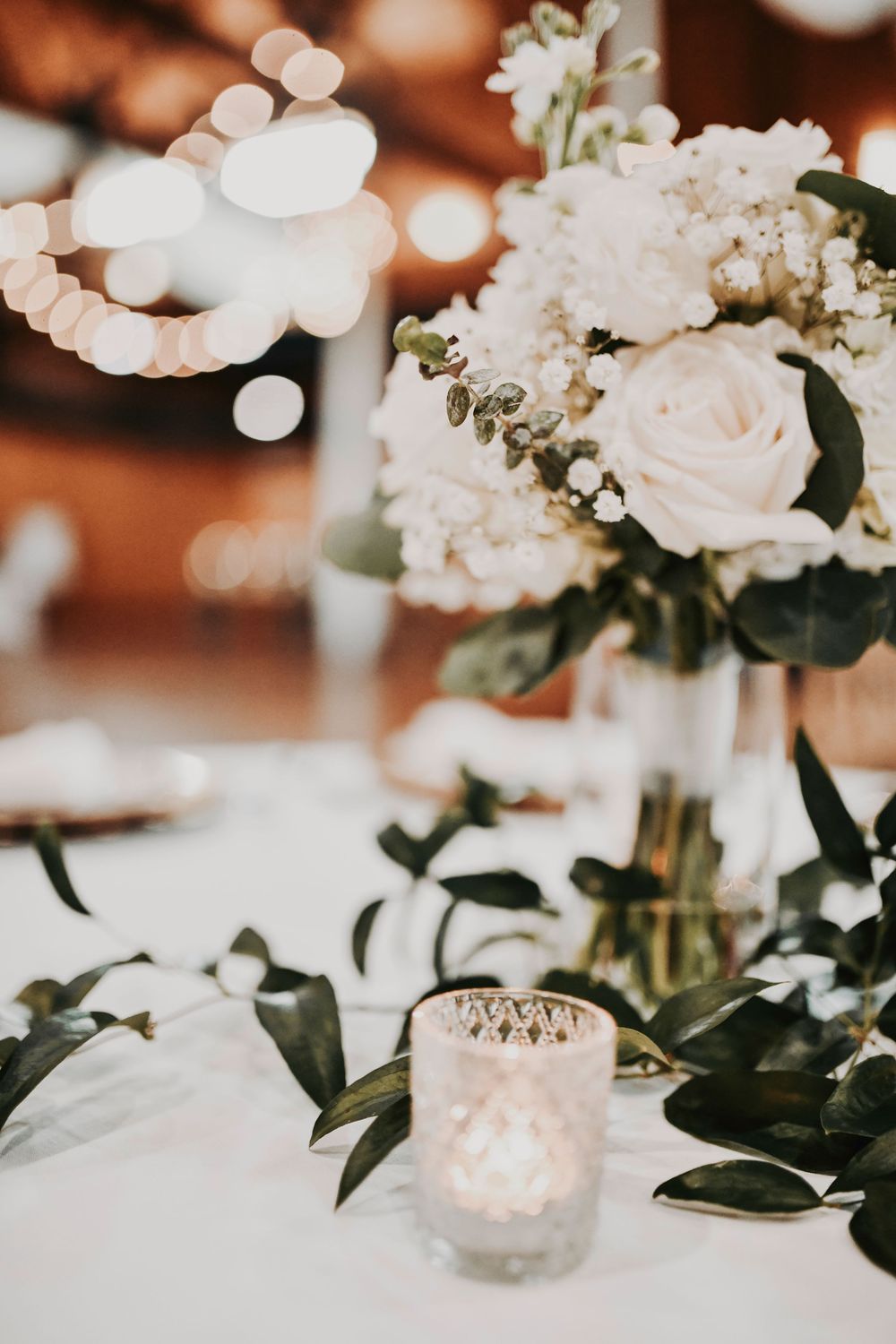 Romantic candlelit reception décor featuring soft sage linens and modern black-tie wedding style.