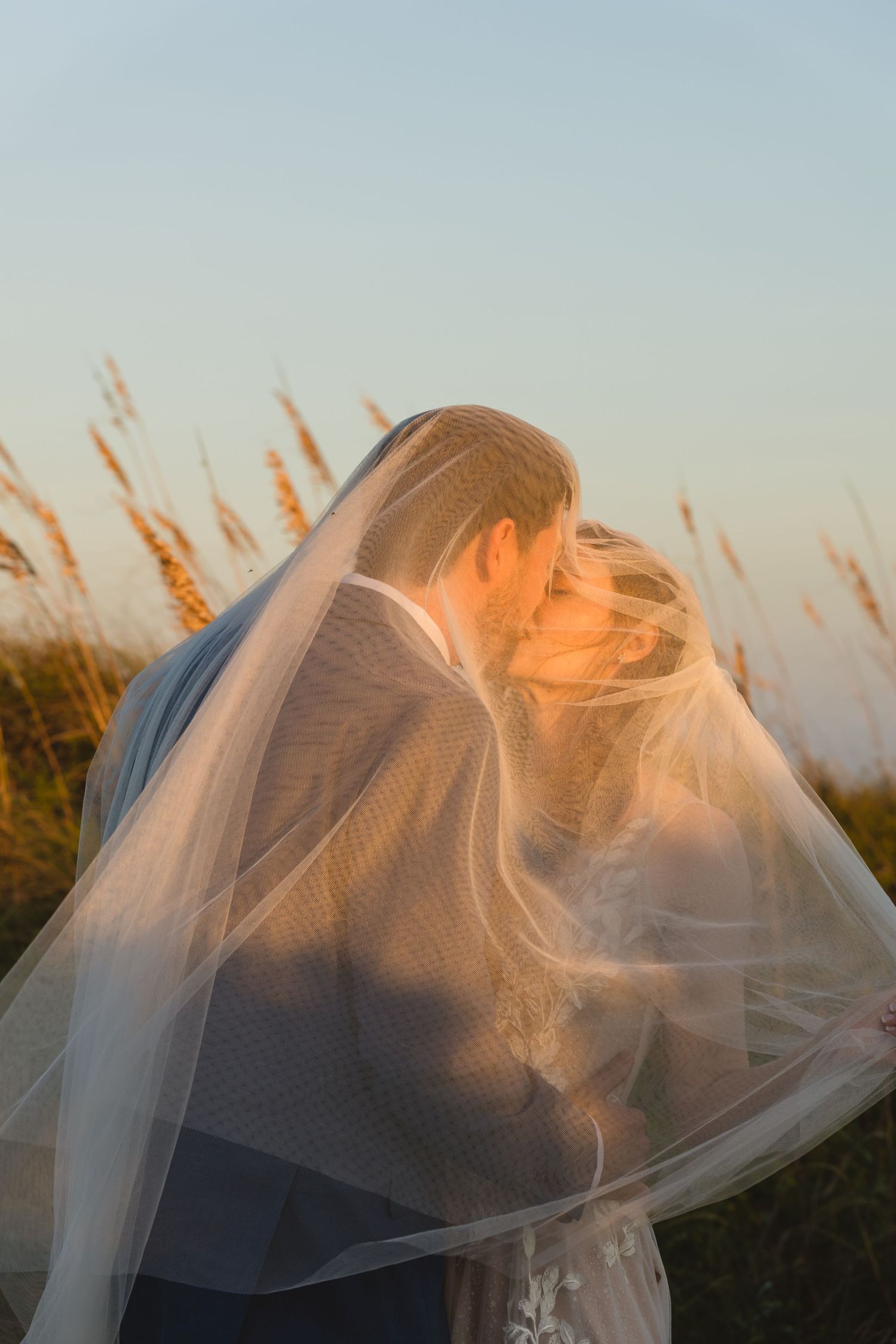 Ethereal wedding portrait with flowing veil against golden sunset light.