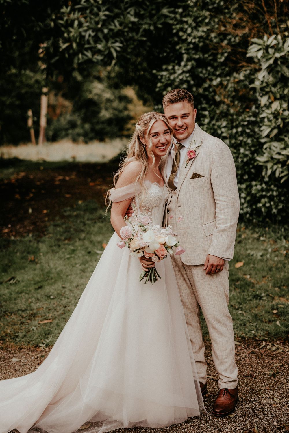 A joyful wedding couple shares candid moments together in a lush garden setting wearing light colored attire.