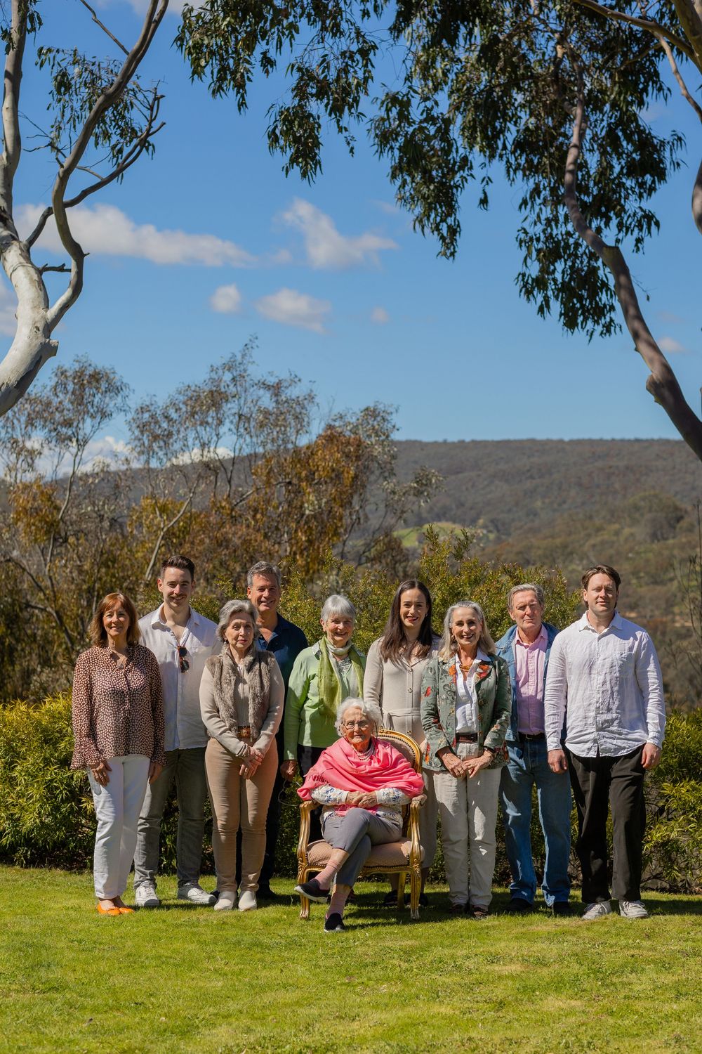 A group of people gathered outdoors on a grassy hillside with eucalyptus trees and mountains in the background.