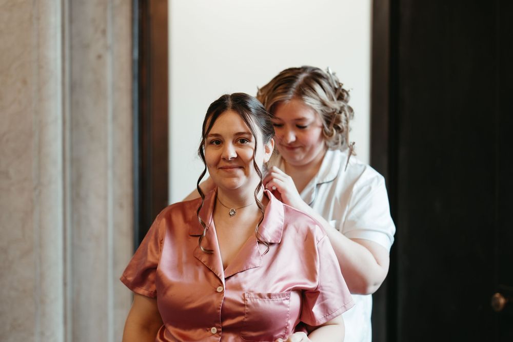 Bridesmaid in pink satin robe getting hair styled by hairstylist during bridal party preparations.