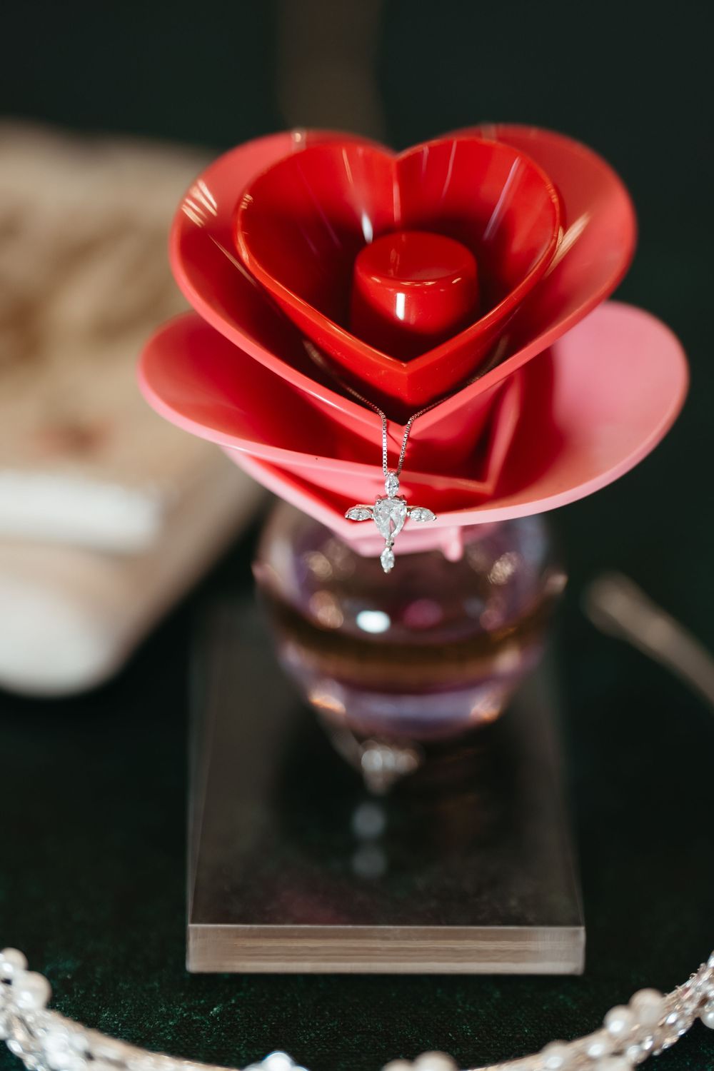 Red heart-shaped origami flower jewelry holder displaying a delicate silver cross necklace on a glass vase base.