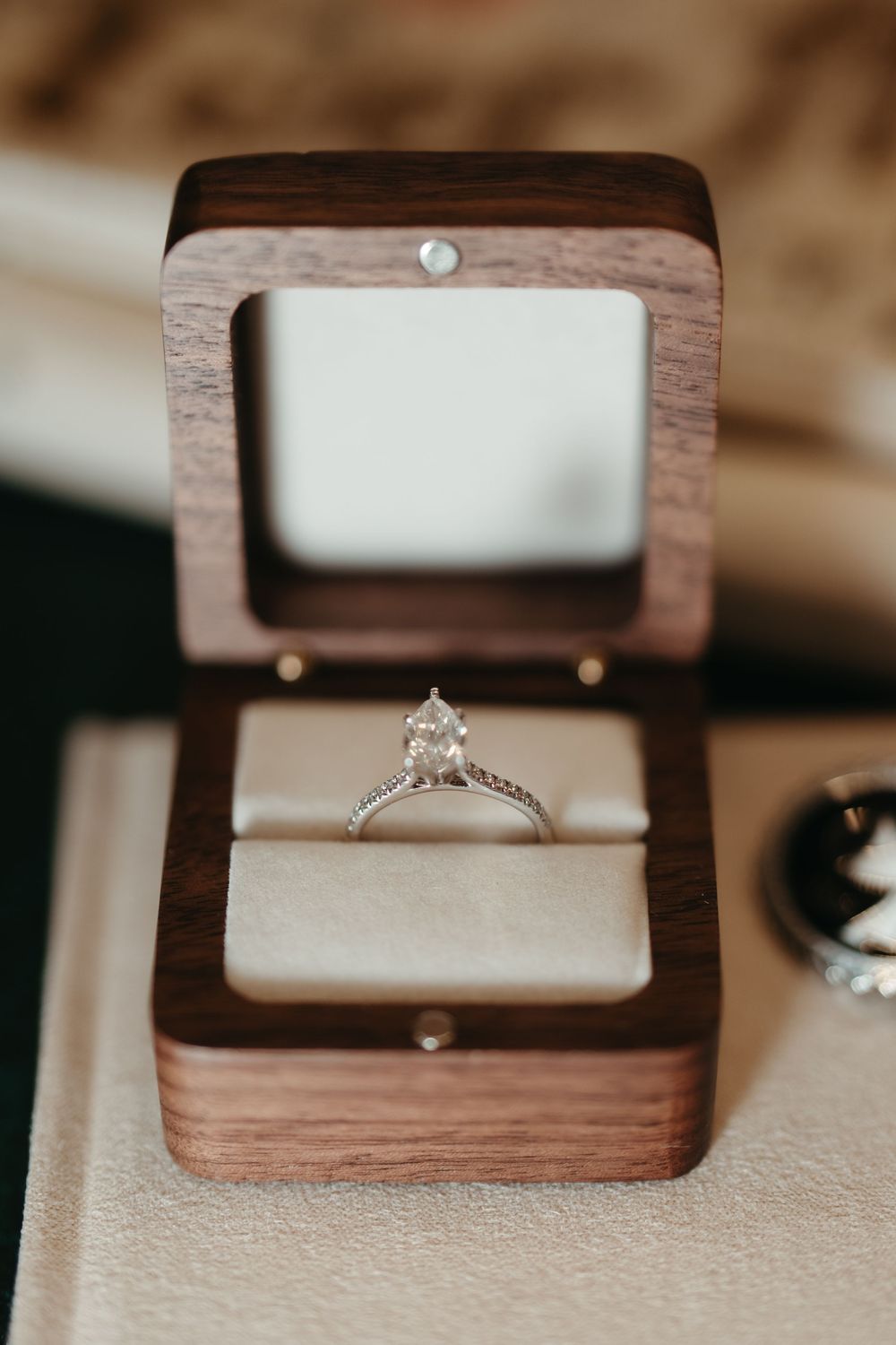Diamond solitaire engagement ring displayed in an open wooden ring box with white velvet interior.