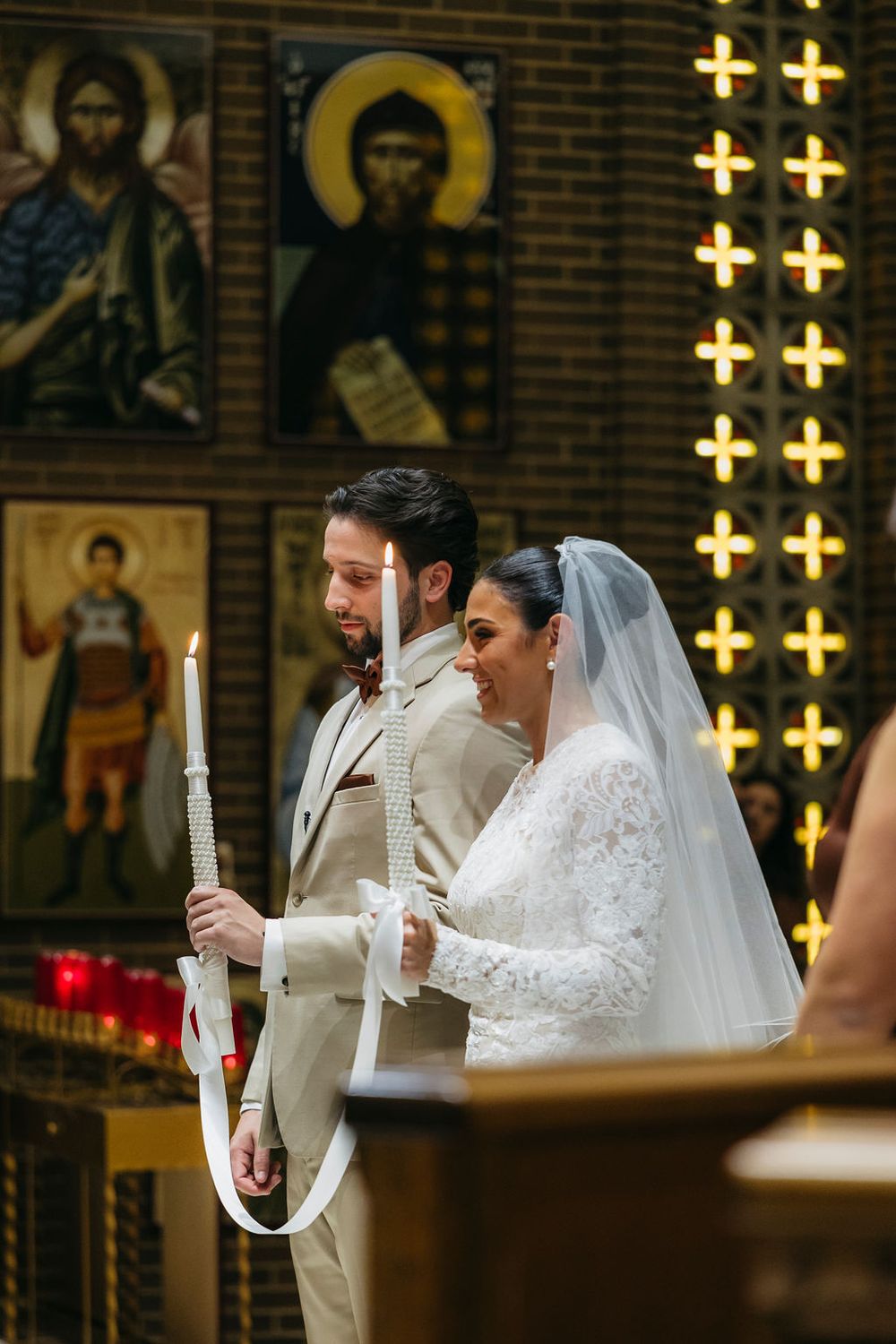Bride and groom holding white candles during an Orthodox Christian wedding ceremony inside a church decorated with icons in Chicago