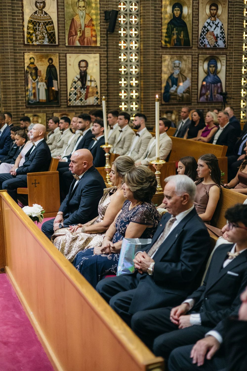 Wedding guests seated in wooden pews during an Orthodox church ceremony surrounded by golden religious icons on the walls in Chicago