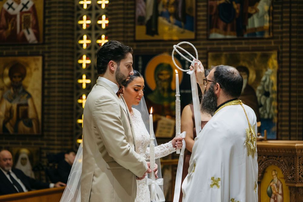 Couple exchanges vows during Orthodox Christian wedding ceremony with priest holding ceremonial cross in ornate church in Chicago