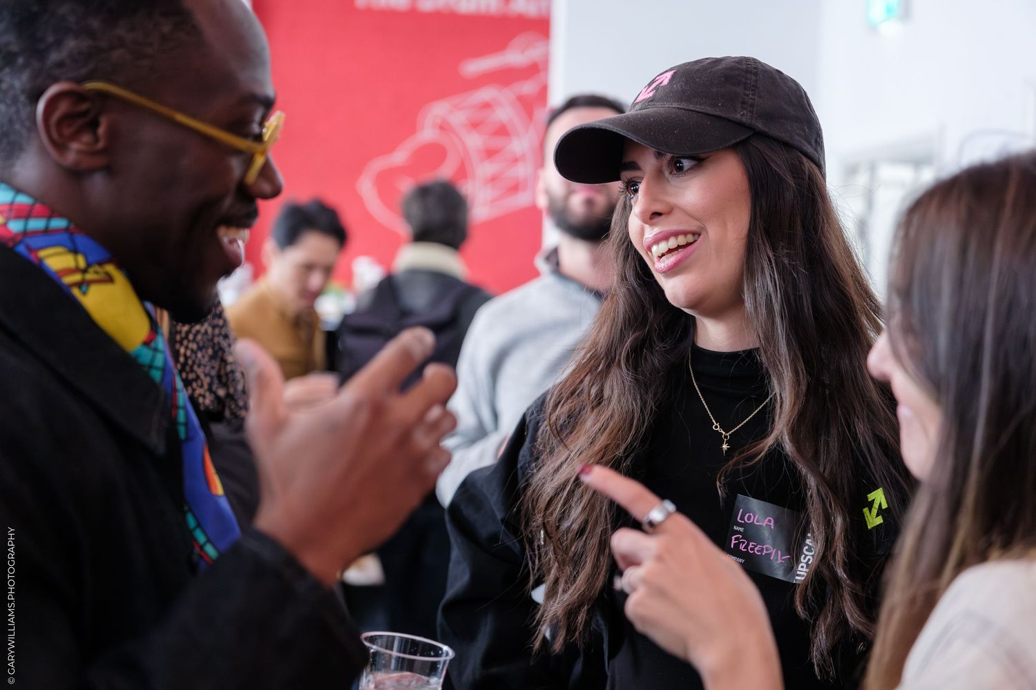 People networking and smiling at a social event, with a woman in a black cap and shirt engaging in conversation.