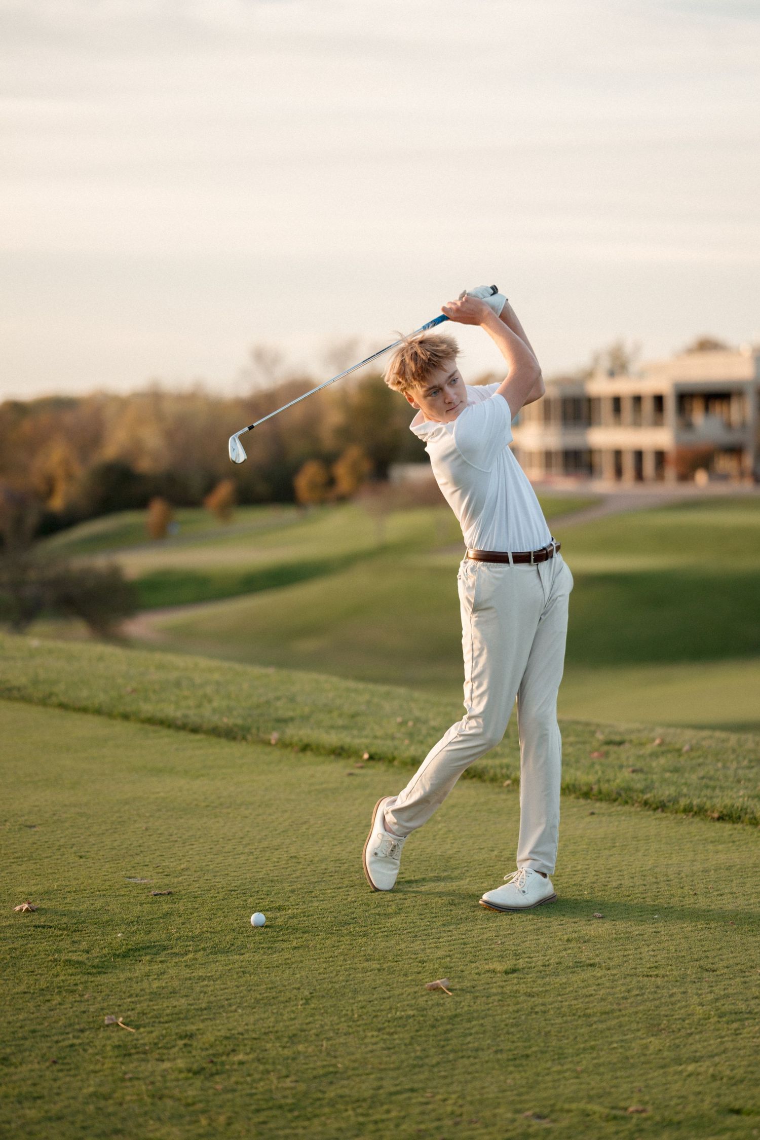 Senior boy golfer in white golf attire photographed at a country club with warm golden light and clean timeless edits.