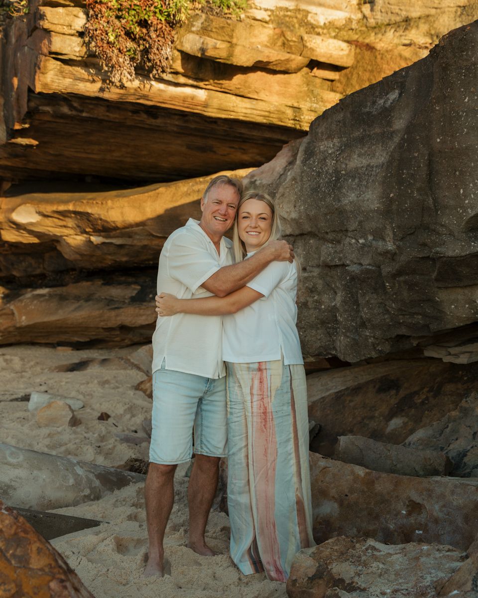 father and young daughter hugging and smiling on a rocky beach with sandstone cliffs at golden hour photoshoot in Bronte Beach Sydney