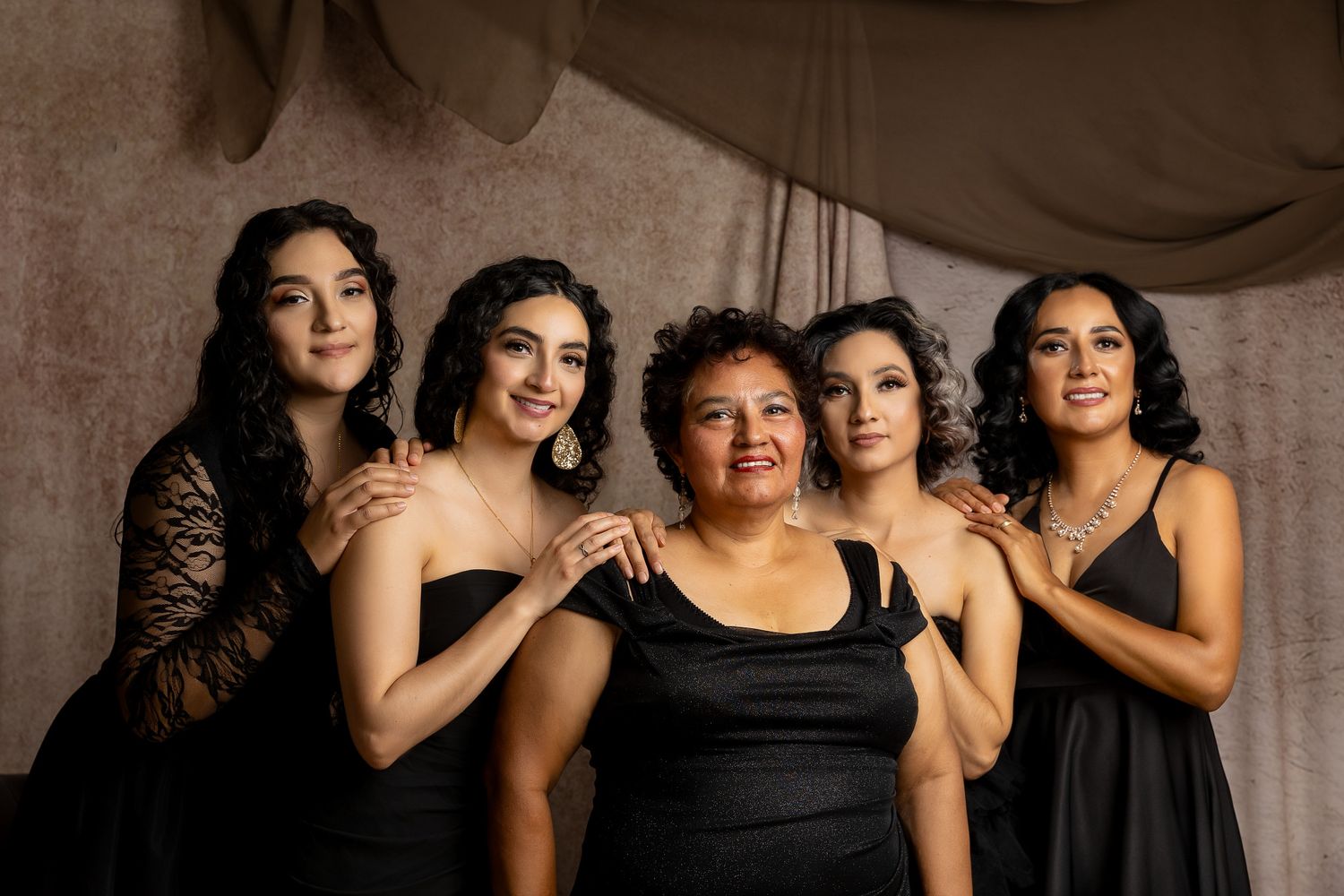 A family of seven poses elegantly in matching black formal attire, with two men in cowboy hats, against a draped studio backdrop.