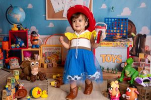 Toddler dressed as Jessie from Toy Story surrounded by colorful toys and Pixar-themed props in a playful photo setup.