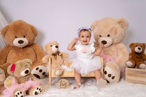 Baby girl in white tutu sits among large teddy bears for a milestone photo session marking her tenth month.