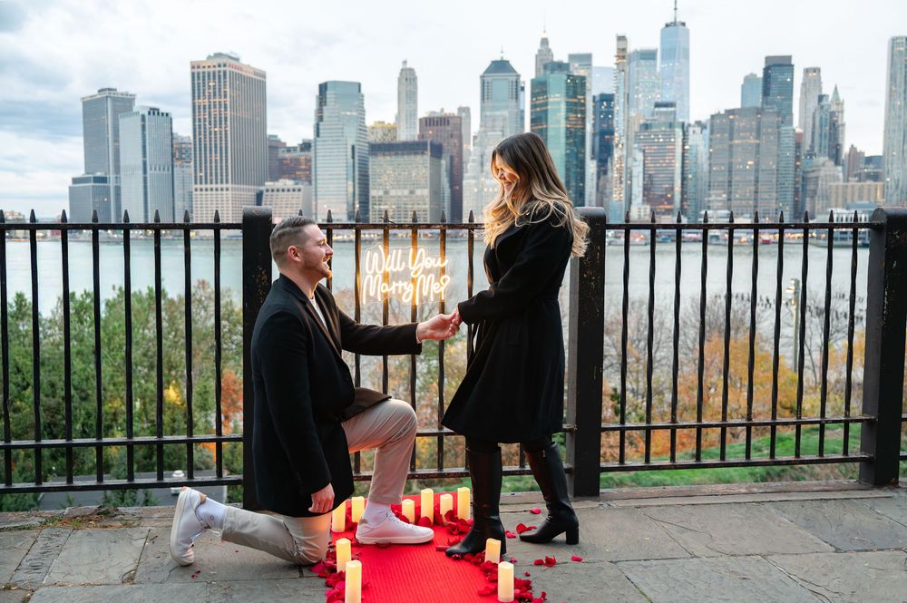 Man proposes on one knee with candles on a rooftop overlooking the NYC skyline.