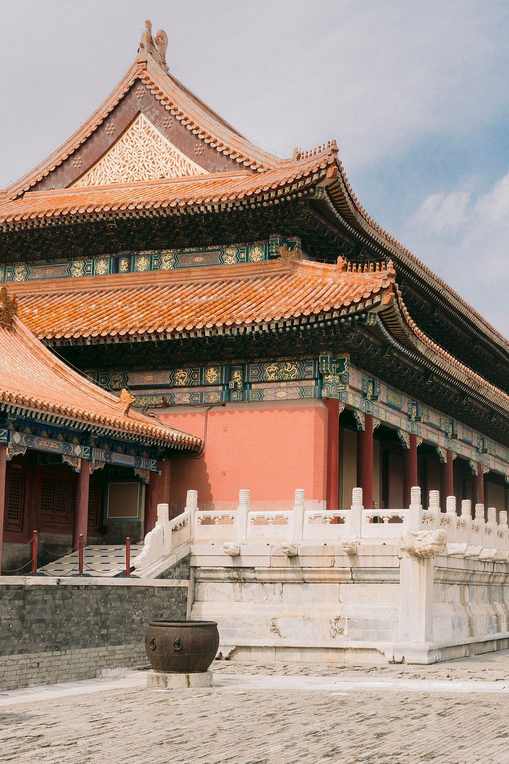 Traditional Chinese imperial palace with ornate golden roof, red walls, and white marble balustrades under a blue sky.