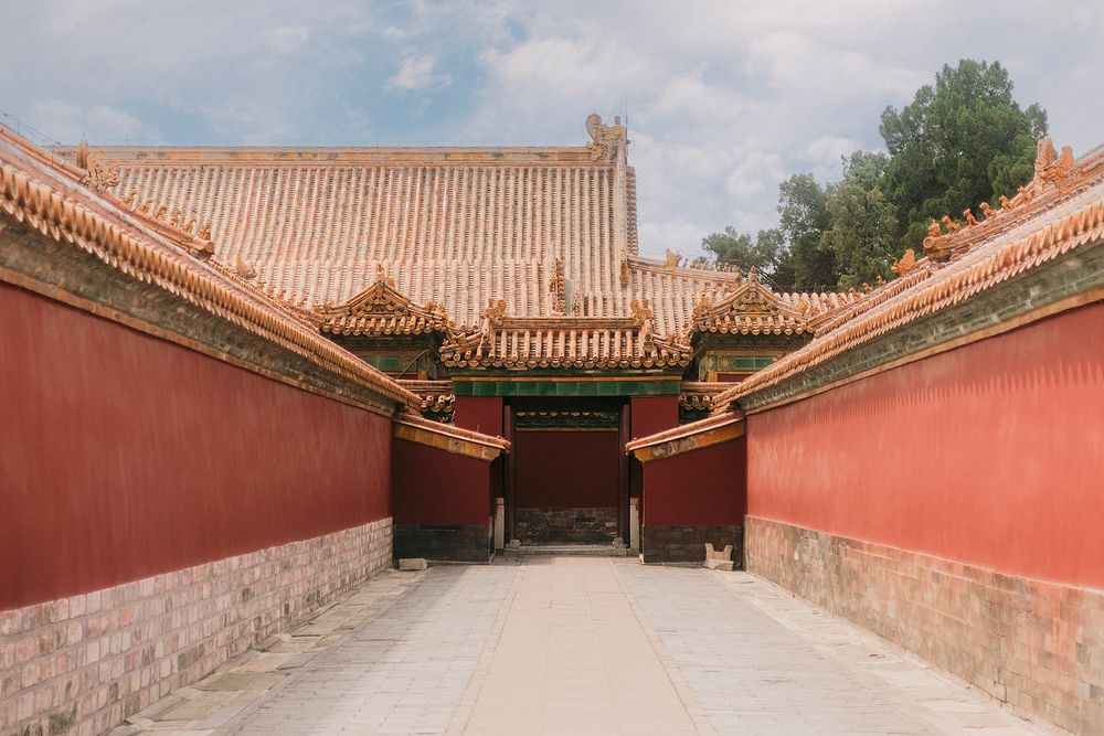 Traditional Chinese architecture with red walls and golden tiled roofs leading to a gate in the Forbidden City.