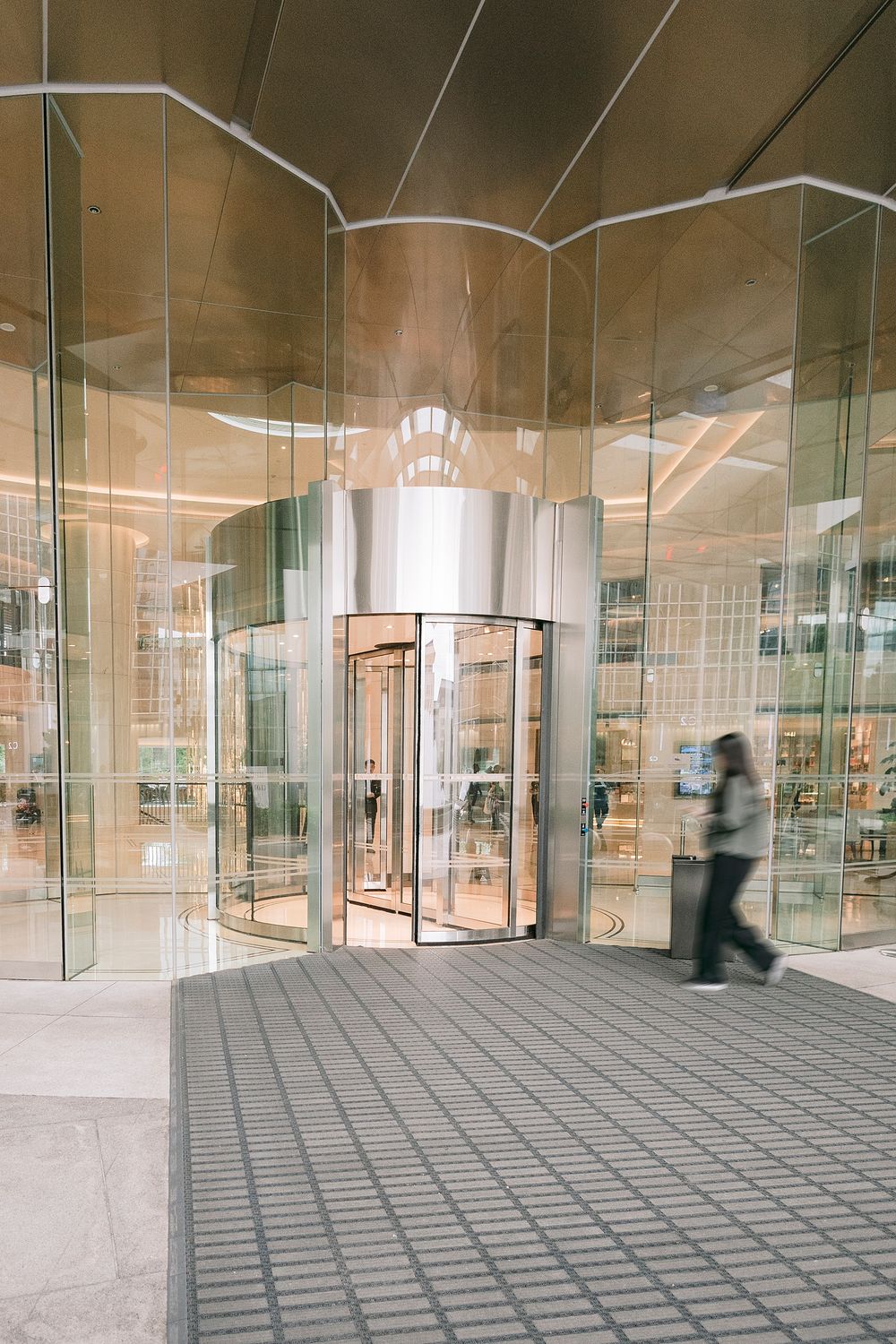 Modern glass building entrance with revolving door and blurred pedestrian walking past reflective facade.