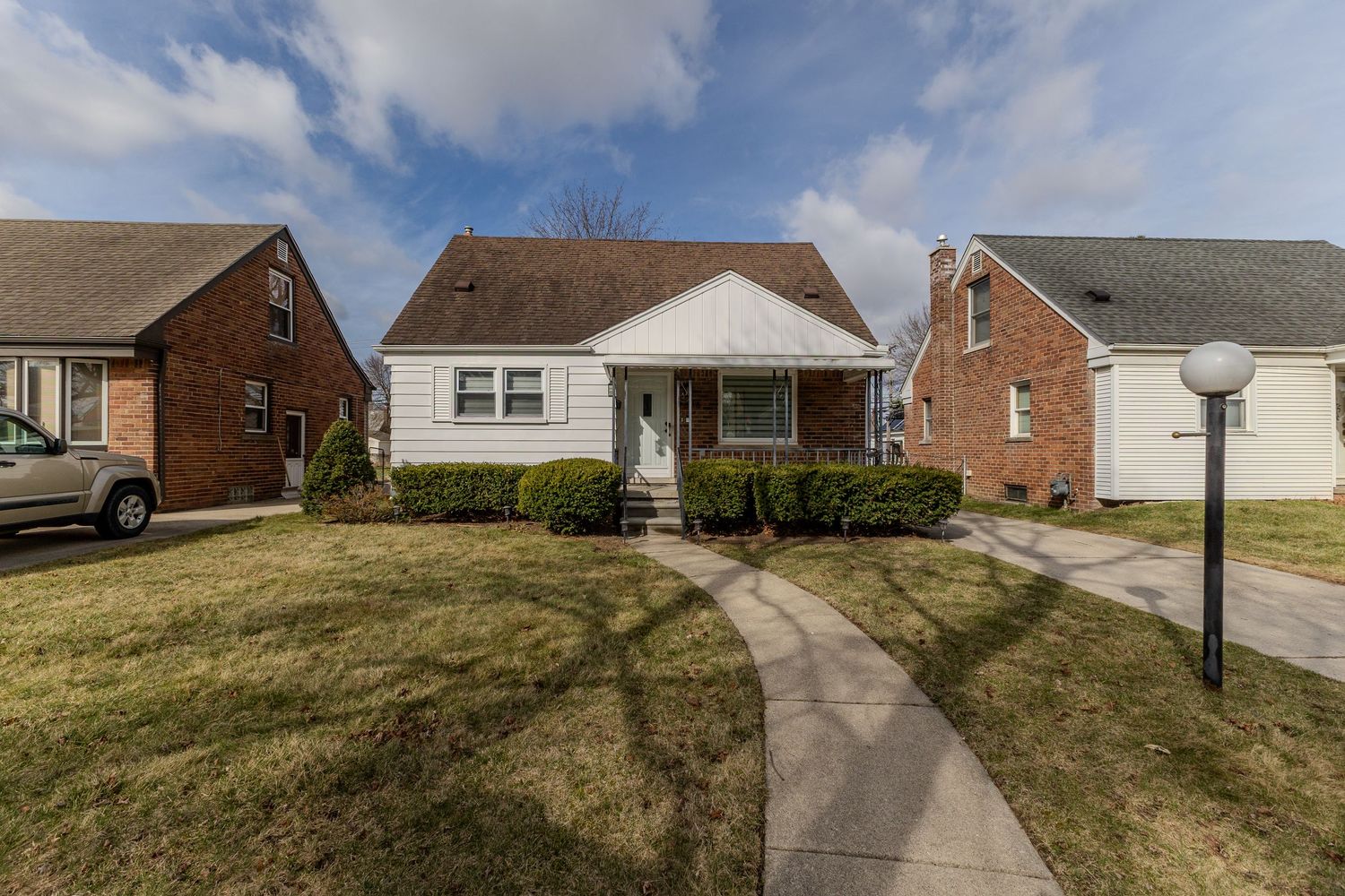 Charming brick bungalow with white siding, covered porch, and well-maintained front lawn.