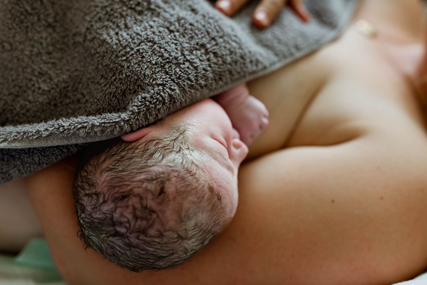 Newborn baby resting on mother's chest covered with a gray towel after birth.