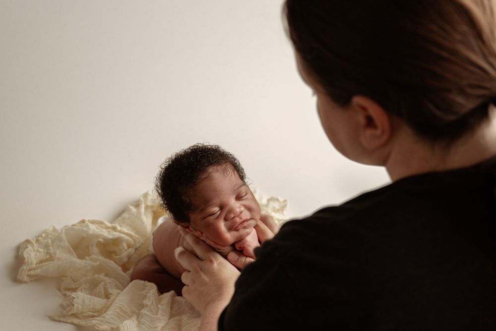 Mother tenderly holding smiling newborn baby wrapped in cream blanket during precious bonding moment.