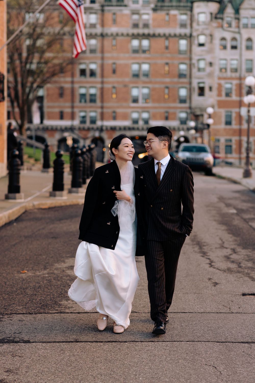 Smiling wedding couple walking together on a cobblestone street with historic building backdrop.