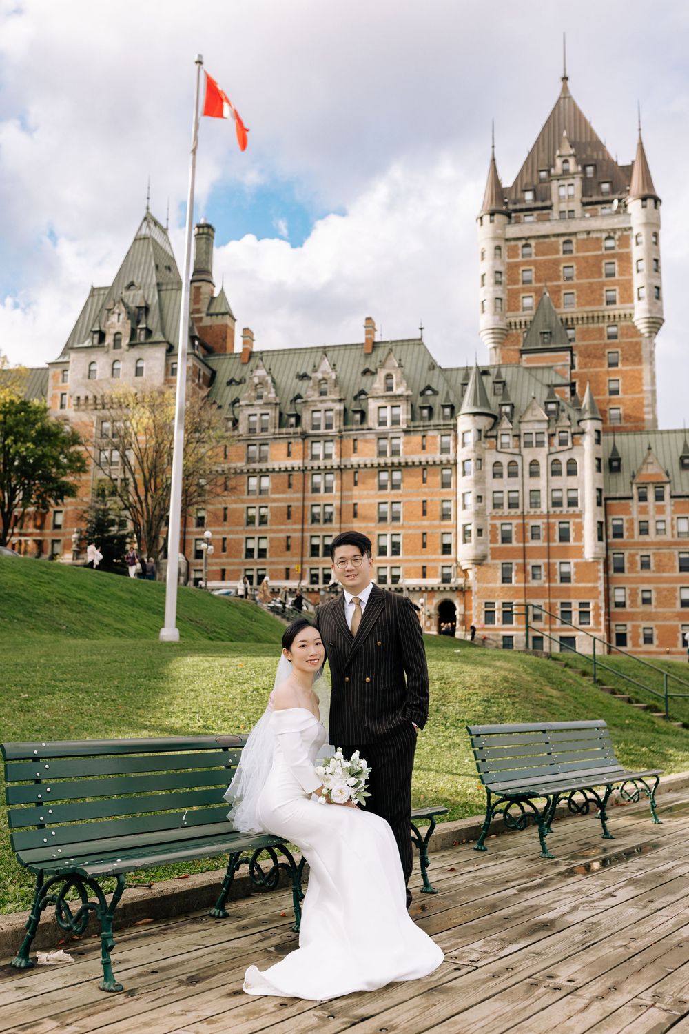 Couple in wedding attire posing in front of Chateau Frontenac in Quebec City with Canadian flag.
