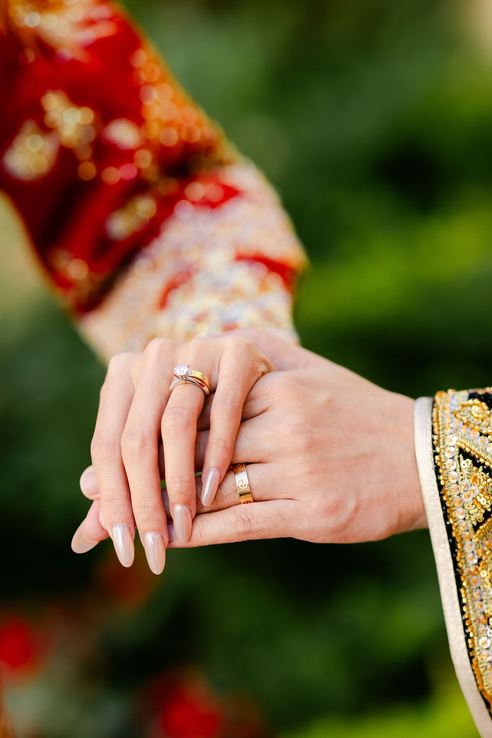 Close-up of a couple holding hands wearing gold wedding rings, dressed in traditional embroidered wedding attire.